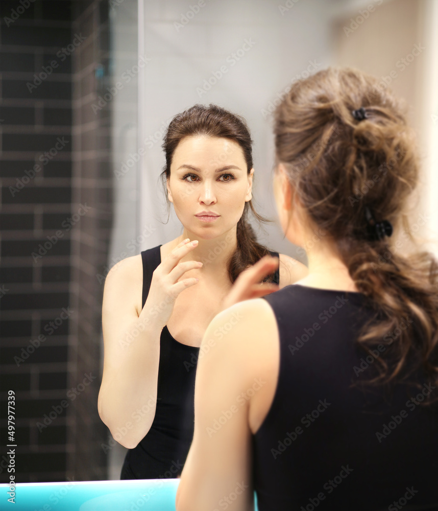 Woman looking in the mirror Applying the cream..Magic anti-aging cream.