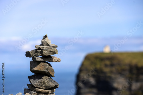 A stack of rocks with the O'Brien tower at the Cliffs of Moher out of focus in the background © bacothelock