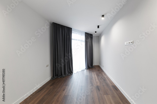 Bright white empty room, stylish interior design of the apartment. Designer gray curtains, brown parquet and white walls. Renovated apartment.