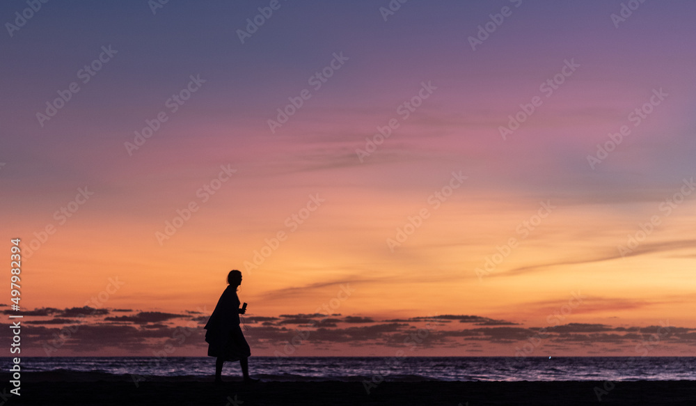 woman walking along the shore of the beach at sunset