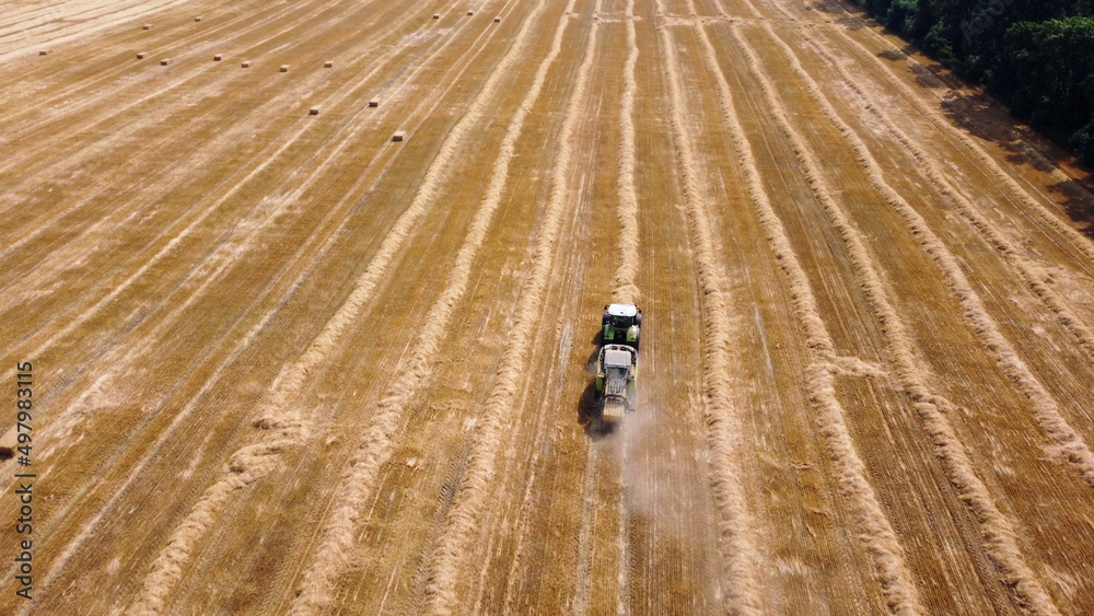 Obraz premium Hay bale tractor. Tractor harvesting hay into bales in field on sunny day. Aerial drone view. Tractor drives across field and makes bales from cut straw. Field and agricultural work, baler. Ukraine