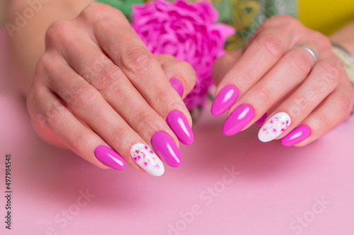 Close up view of beautiful female hands with romantic manicure nails, pink gel polish, peonies flowers design
