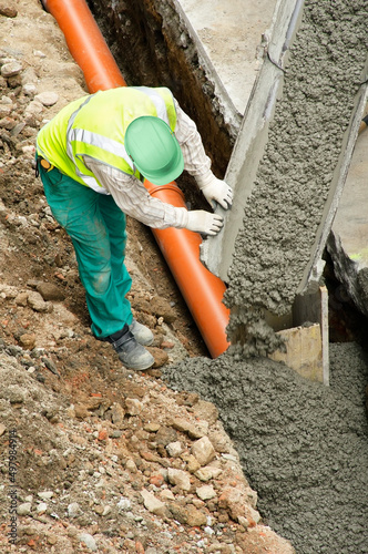 worker installing sewer pipes at construction site on street city