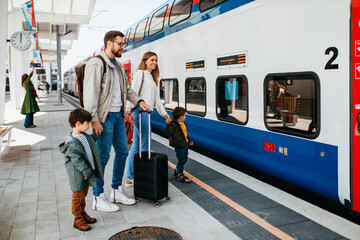 Happy ypung family with luggage in railroad station go together on vacation.