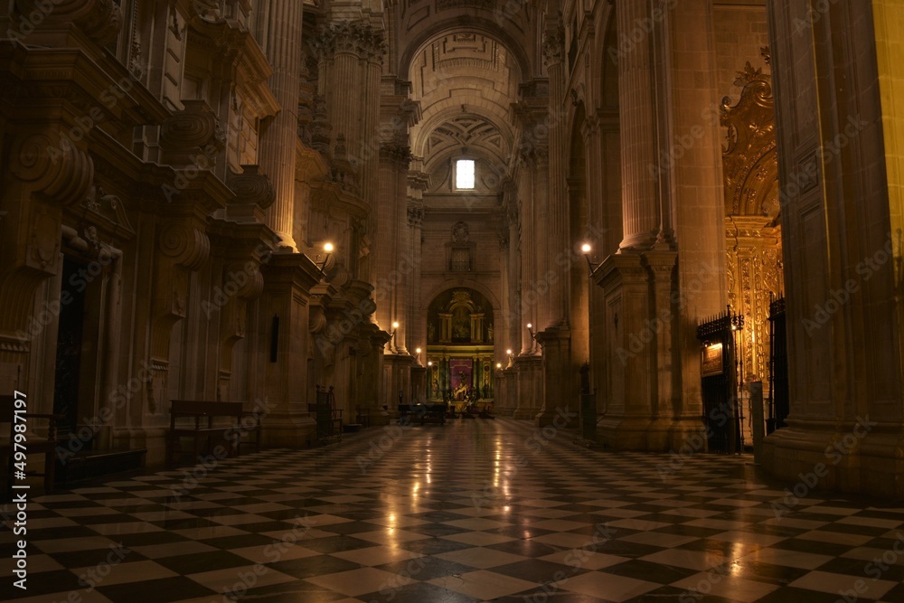 View down the splendid Southern nave of Jaén Cathedral towards Capilla de Santiago chapel lined by columns and reflecting in a shiny checkered black white stone floor, Jaén, Spain