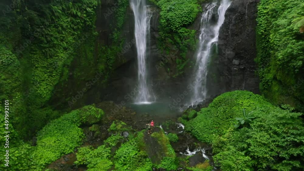 young couple in north bali indonesia standing on top of a rock with two large waterfalls called sekumpul in the middle of a tropical jungle young couple in north bali indonesia standing on top of a rock with two large waterfalls called sekumpul in the middle of a tropical jungle