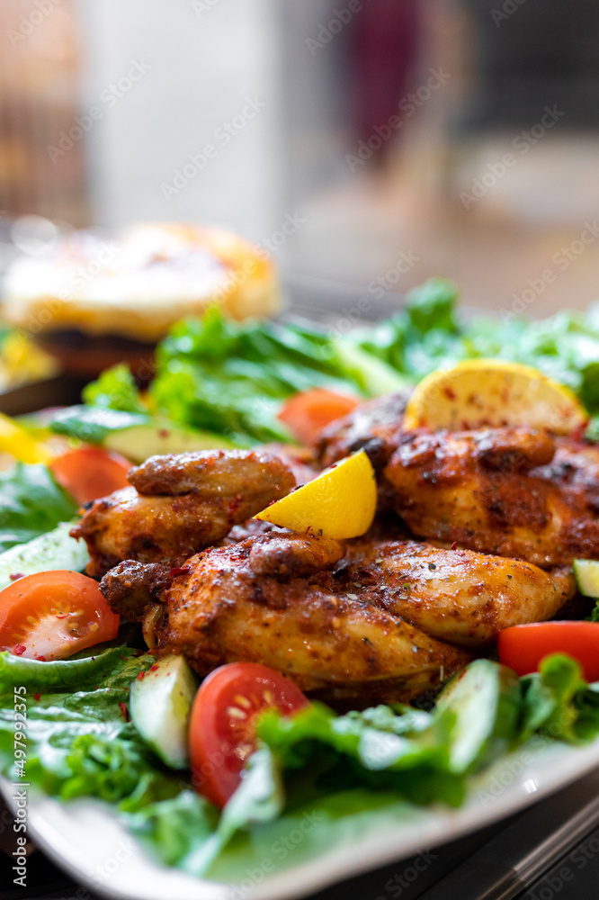 Tobacco chicken with lettuce, lemon and tomato in a white plate. Selective focus, vertical copy space