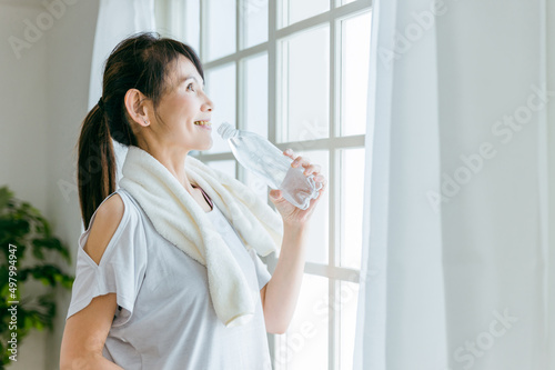室内でトレーニング後にペットボトルの水を飲む中高年女性（水分補給） 