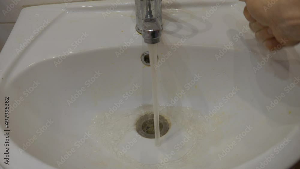 Dirty yellow water flows from the faucet into the sink. A man's hand opens a faucet with hot dirty water. Selective focus. problems with tap water in the city Dirty yellow water flows from the faucet into the sink. A man's hand opens a faucet with hot dirty water. Selective focus. problems with tap water in the city