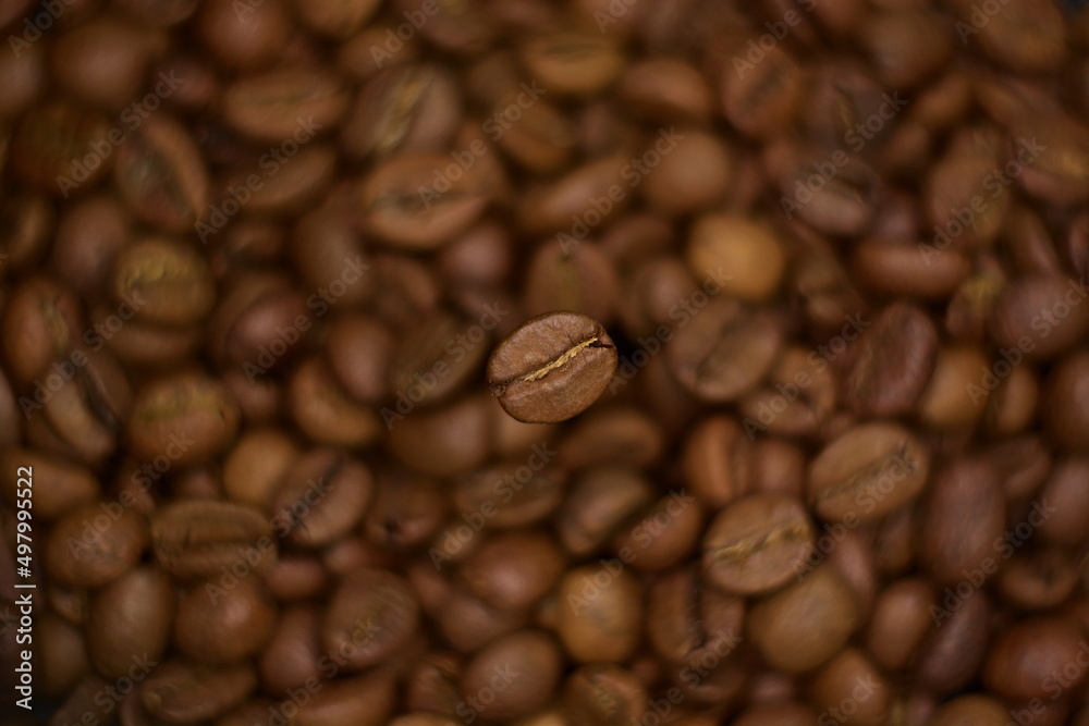 Obraz premium Top view on natural roasted coffee bean close up hovering in frozen motion on blurry background of coffee beans. Selective soft focus, twisted bokeh effect