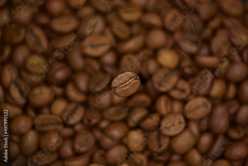 Top view on natural roasted coffee bean close up hovering in frozen motion on blurry background of coffee beans. Selective soft focus, twisted bokeh effect