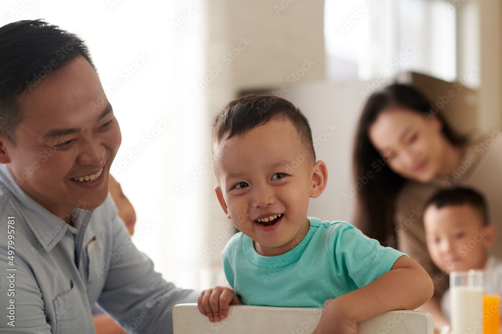 Smiling father looking at little boy sitting on chair at breakfast table Smiling father looking at little boy sitting on chair at breakfast table