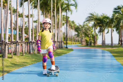 asian child or kid girl playing skateboard or surf skate in skating rink track and extreme sports exercise to wearing helmet elbow pads wrist and knee support for body safety protect at bang phra park