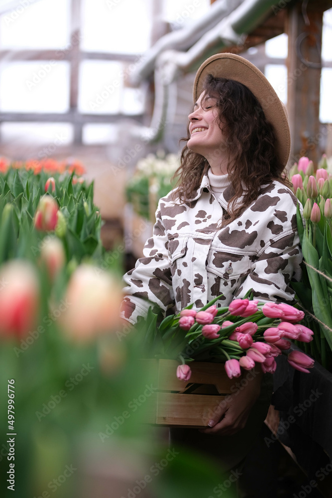 Young girl farmer in hat holds a box with bouquets of tulips of in her hands. Caucasian woman demonstrates the products of a small family-owned flower growing business