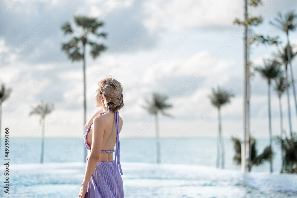 Woman in purple dress posing by the pool with sea view.