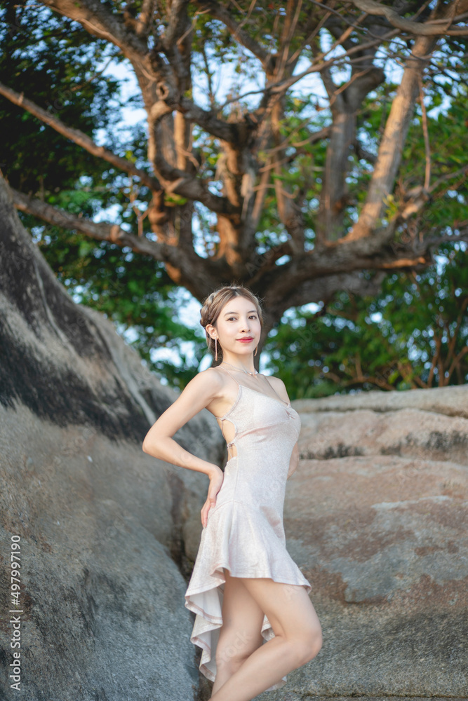 Woman wearing short glitter dress enjoying romantic moment at the beach, standing near big rock. Woman wearing short glitter dress enjoying romantic moment at the beach, standing near big rock.
