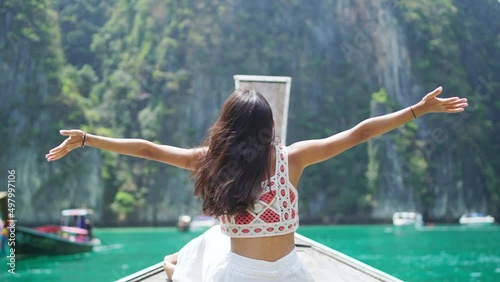 Young beautiful Asian woman in blue dress sitting on the boat passing island beach lagoon in summer sunny day. Happy female relax and enjoy outdoor lifestyle together on summer vacation in Thailand