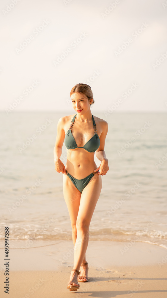Woman in green bikini walking on beach.