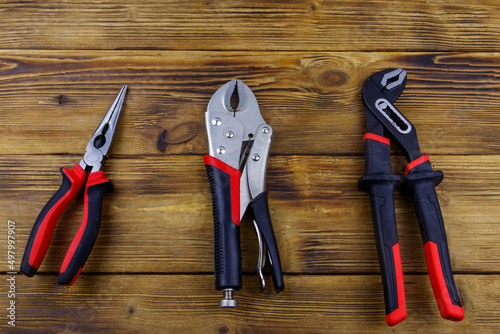 Set of different pliers on wooden background. Top view photo