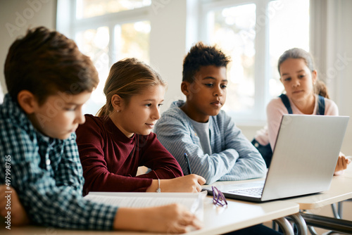 Group of elementary school classmates e-learning on laptop in classroom.