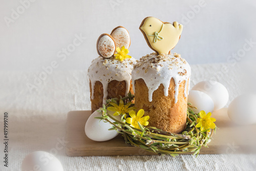 Traditional easter cake decorated with easter cookies, willow twigs in shape of nest, yellow flowers, white eggs on linen tablecloth. Side view, selective focus. Easter treat, holiday symbol