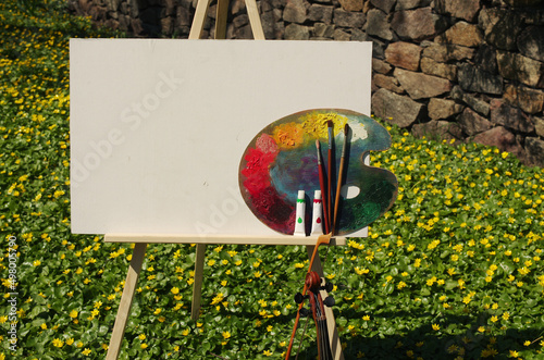 Artist tripod, canvas and palette on the background of a flowering meadow. Place for an inscription. Copy space.