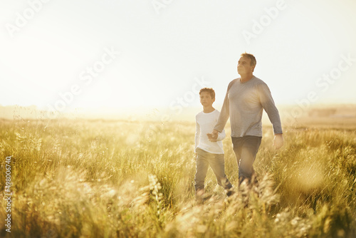 Showing him the beauty of nature. Shot of a man taking his son for a walk out on an open field.