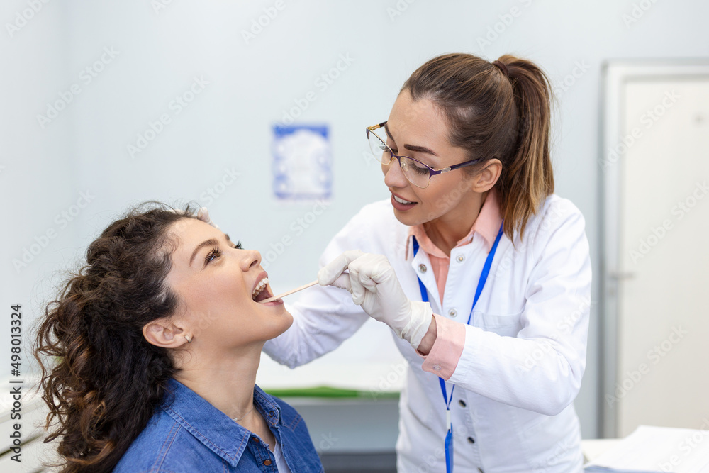 Doctor using inspection spatula to examine patient throat. ENT doctor doing throat exam of a woman. patient opened her mouth to throat check-up Doctor using inspection spatula to examine patient throat. ENT doctor doing throat exam of a woman. patient opened her mouth to throat check-up