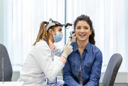 Hearing exam. Otolaryngologist doctor checking woman's ear using otoscope or auriscope at medical clinic. Otorhinolaryngologist pulling ear with hand and looking at it with otoscope closeup. photo