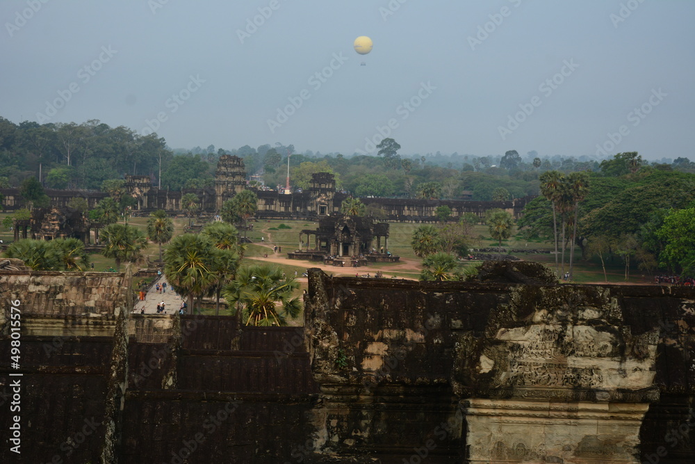 The ancient ruins of Angkor Wat with a hot air balloon in the distance overflying the jungle surrounding the temple grounds
