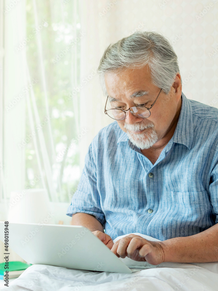 Senior man using a laptop computer smiling feel happy in bed at home - lifestyle senior concept Senior man using a laptop computer smiling feel happy in bed at home - lifestyle senior concept