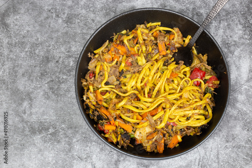 Shredded duck stir fry with spices and vegetables in a black bowl. On a stone background
