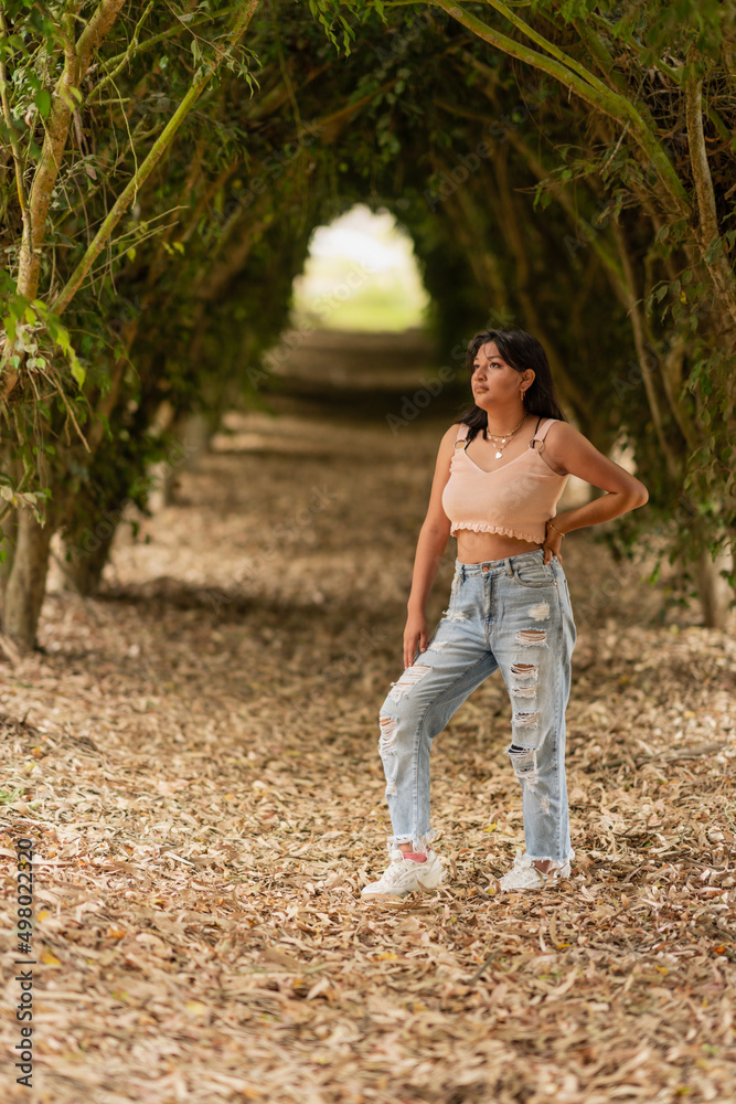 Naklejka premium Woman standing in a tunnel of trees with fallen leaves on the ground