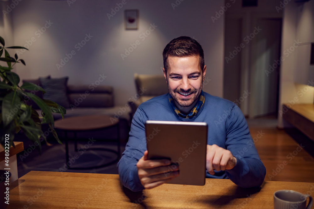 A happy man scrolling on the tablet while sitting at cozy home.