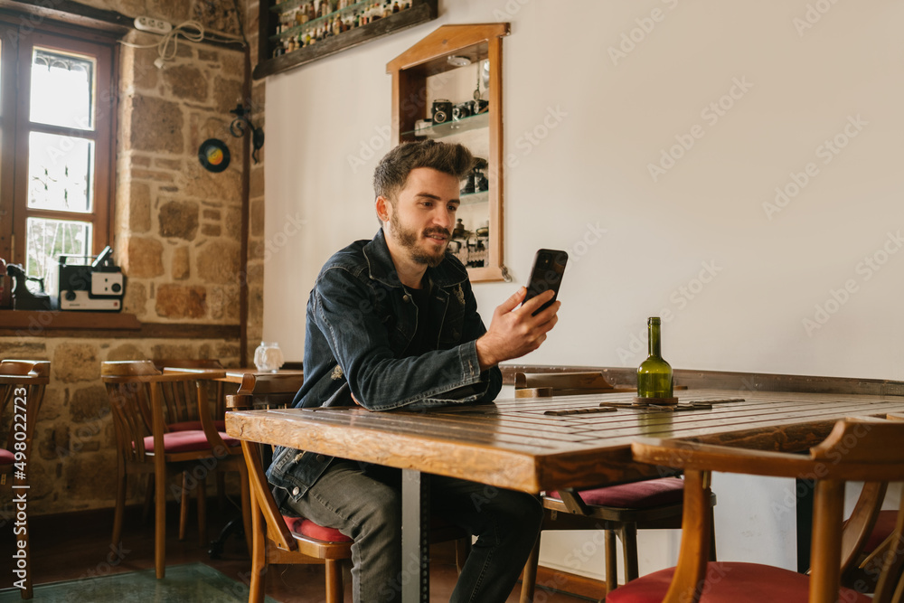 Young man puts his arms on a wooden table and looks at the phone in his hand, an old cafe and a nostalgic look, wood tones and aesthetic place Young man puts his arms on a wooden table and looks at the phone in his hand, an old cafe and a nostalgic look, wood tones and aesthetic place
