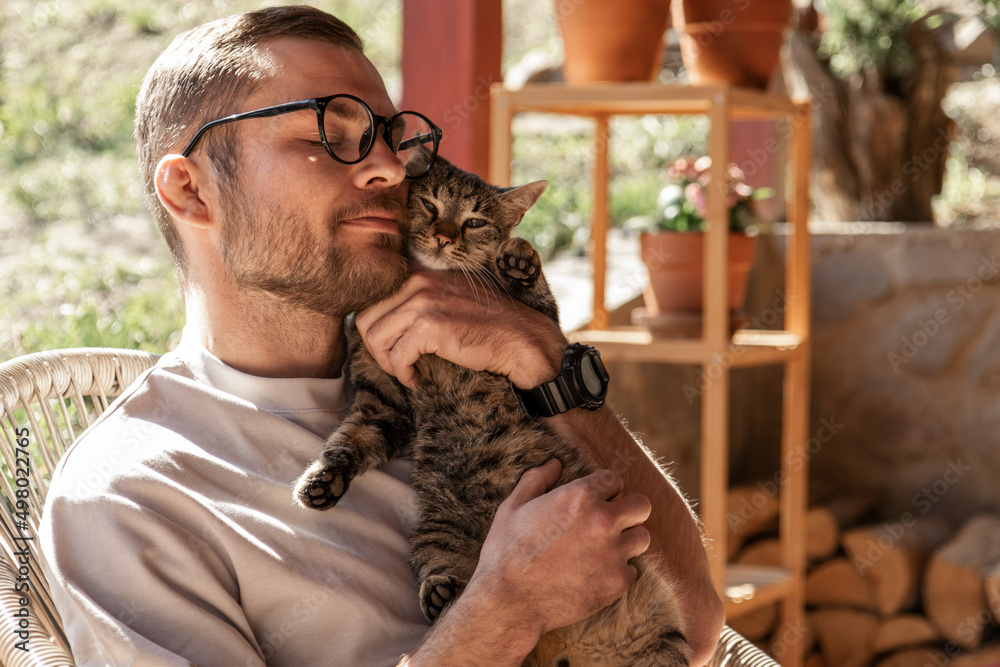 Happy handsome young adult man in glasses cuddles his cute cat. Happy handsome young adult man in glasses cuddles his cute cat.