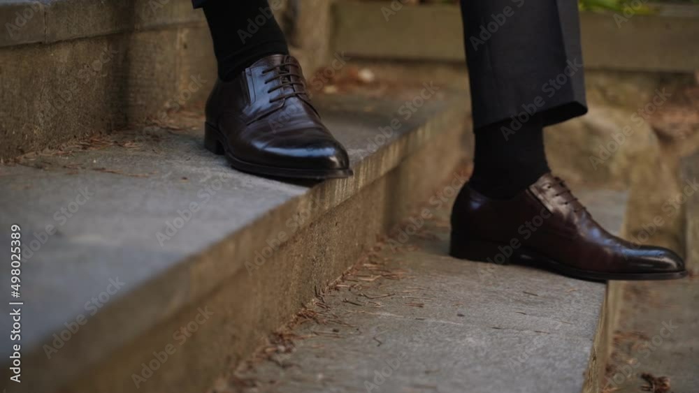 Man in dark brown leather shoes, black socks and gray trousers sits on a dirty concrete staircase in the old quarter and puts his foot on another step. Man in dark brown leather shoes, black socks and gray trousers sits on a dirty concrete staircase in the old quarter and puts his foot on another step.