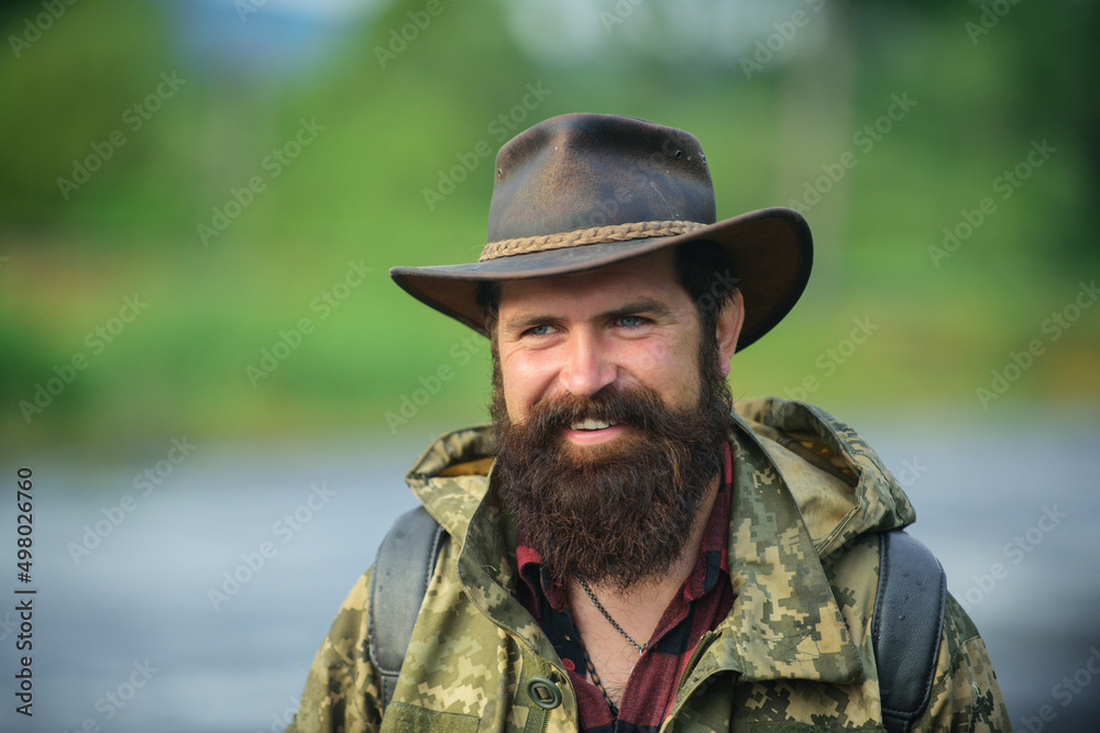 Portrait of traveller bearded man in cowboy hat. Close up portrait of happy middle aged smiling man in a countryside.
