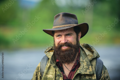 Portrait of traveller bearded man in cowboy hat. Close up portrait of happy middle aged smiling man in a countryside.