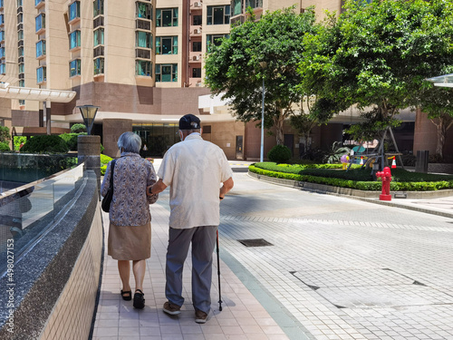 back view of old spouses on a walk with stick in residential area, Hong Kong. Grandfather holding grandmother's hand. Support and care to each other in old marriage couple. Healthcare for Elderly