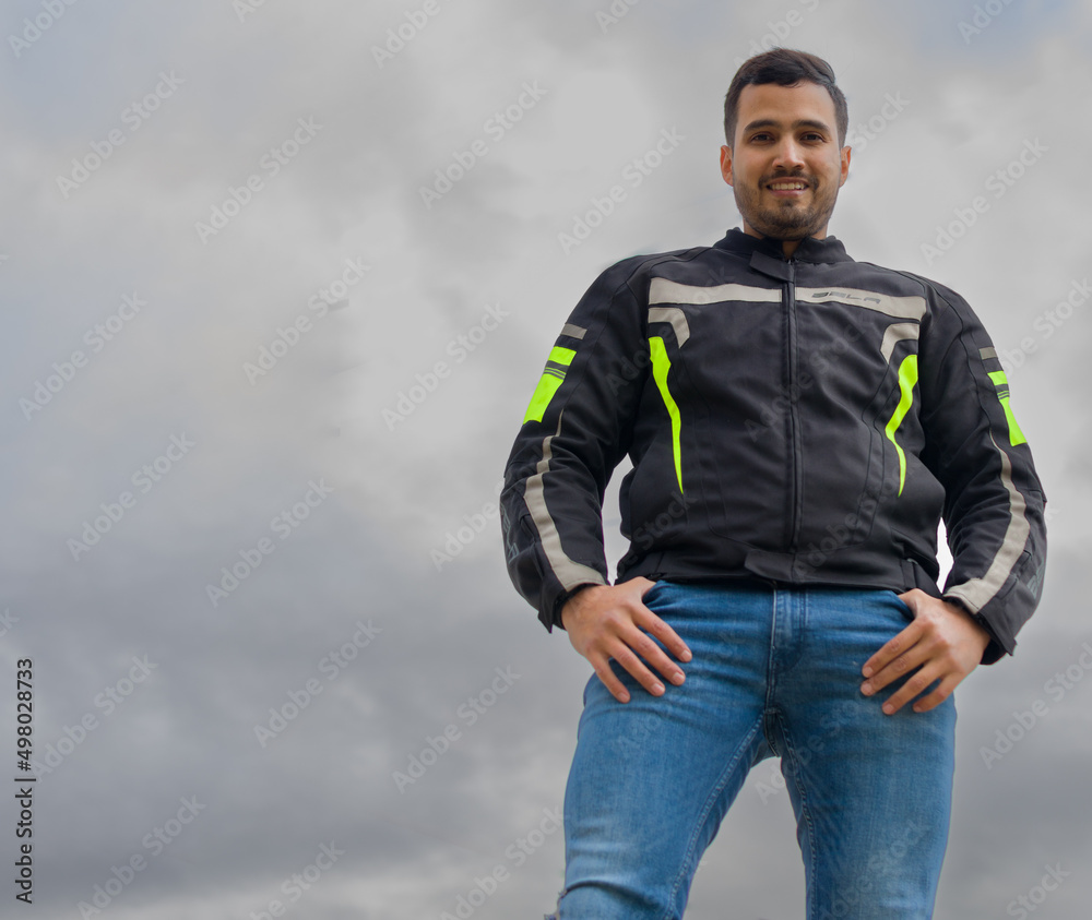 low-angle three quarter length of a colombian-features young man standing with hands in pockets who is looking and smiling down at the camera ahead a cloudy sky low-angle three quarter length of a colombian-features young man standing with hands in pockets who is looking and smiling down at the camera ahead a cloudy sky