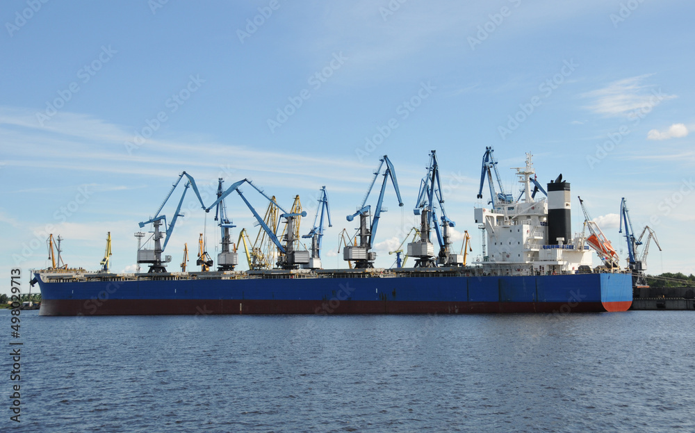 Blue and red ship loaded by port cranes with bulk material in a sea harbor