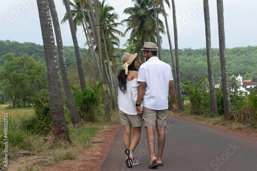 A beautiful young lovely attractive couple looking at each other, embracing, making love, smiling, cuddling walking on a famous Parra Coconut road in Goa surrounded by or lined with palm trees fields.