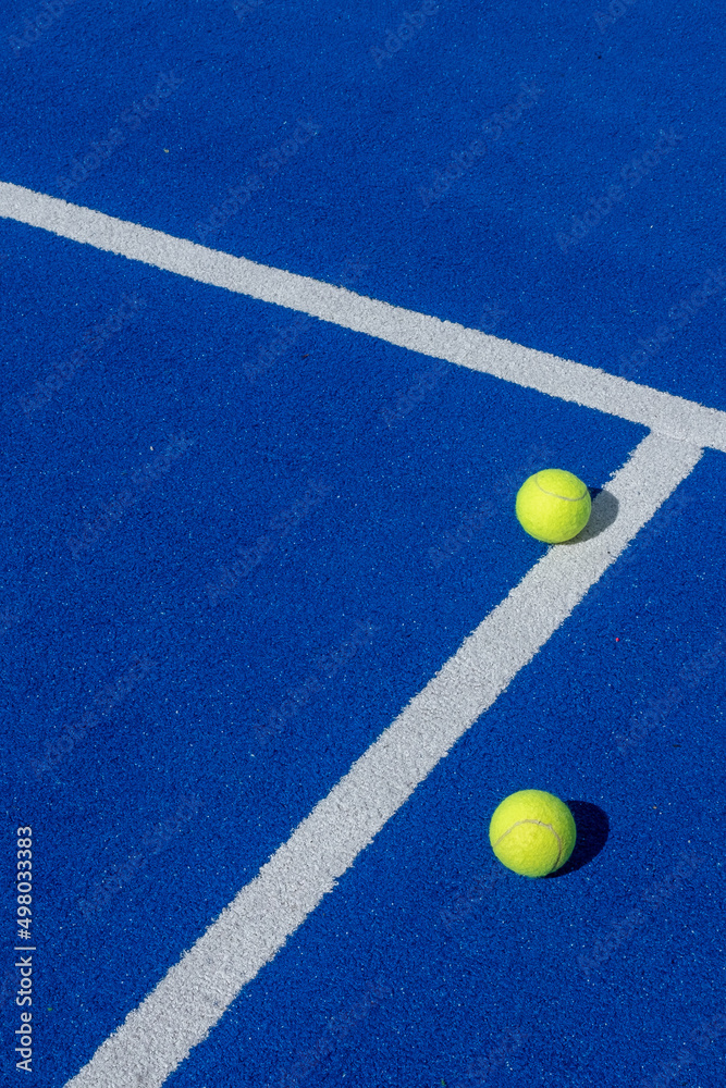 two balls next to the lines of a blue paddle tennis court