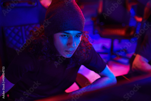 Concentrated young app developer or hacker using computer in dark blue room