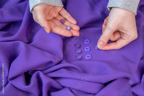 The girl applies buttons of matching color to the purple fabric. Hobby, sewing.