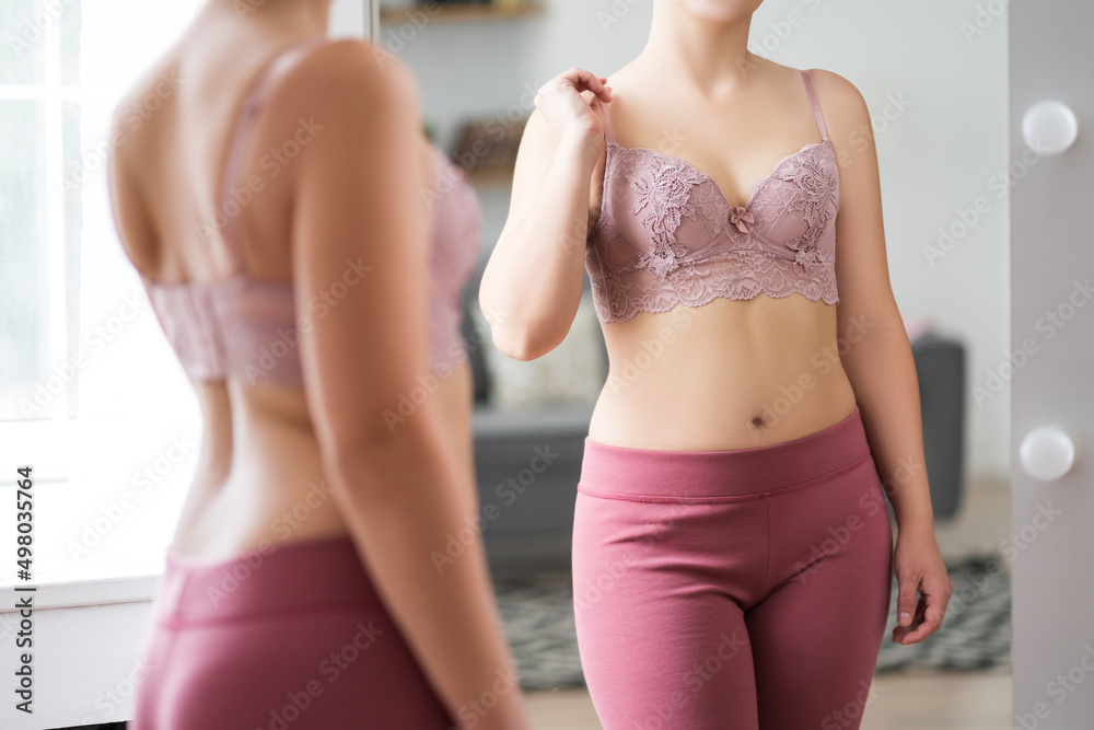 A woman tries on a bra in the fitting room, a bustier with a wide clasp is  reflected in the mirror Stock Photo
