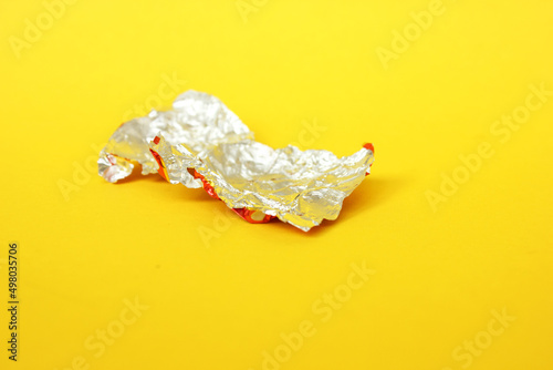 packaging made of aluminum foil without chocolates on a yellow background. Texture of used mint aluminum food foil. A piece of paper from a candy. Garbage. Copy space