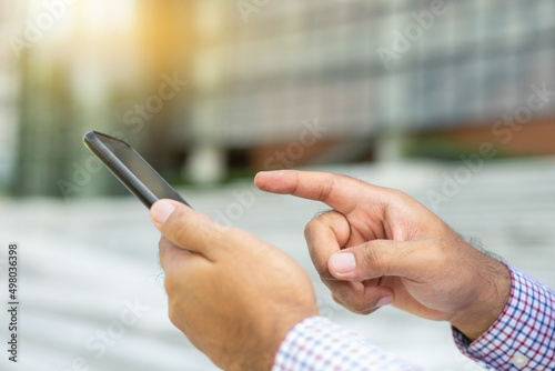 Close up businessman using modern smartphone device typing text message in social media while sitting on stairs outdoor. Happy male spending free time in break of working. photo