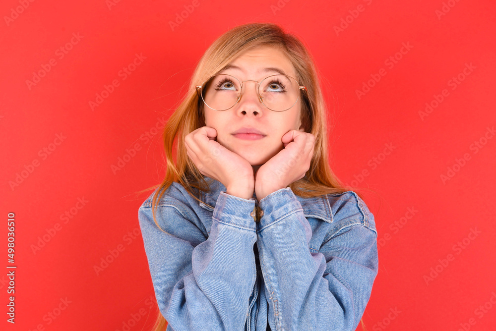 Portrait of sad blonde little kid girl wearing denim jacket over red background hands face look empty space Portrait of sad blonde little kid girl wearing denim jacket over red background hands face look empty space